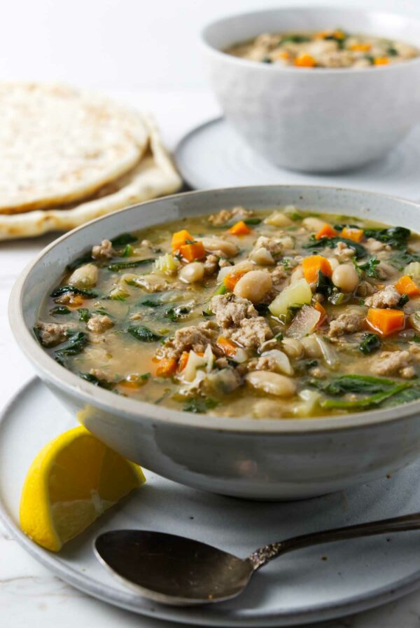 A bowl of white bean soup with chicken and veggies; a lemon wedge next to the soup.