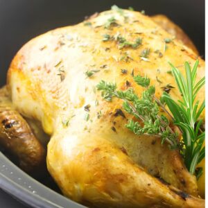 Whole roasted chicken with herbs in a black slow cooker.
