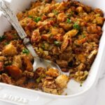 A spoon scooping a serving of fennel stuffing from a casserole dish.