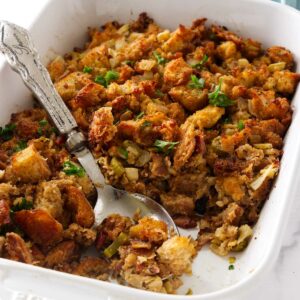 Stuffing with fennel and bacon in a white dish with a spoon.