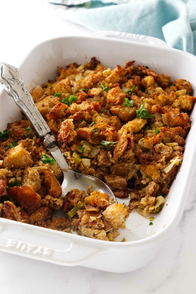 Stuffing with fennel and bacon in a white dish with a spoon.