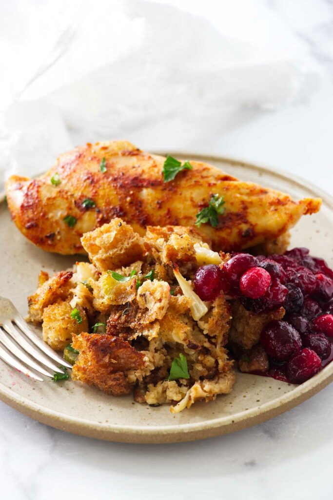 Stuffing with parsley and cranberry sauce on beige plate with turkey.