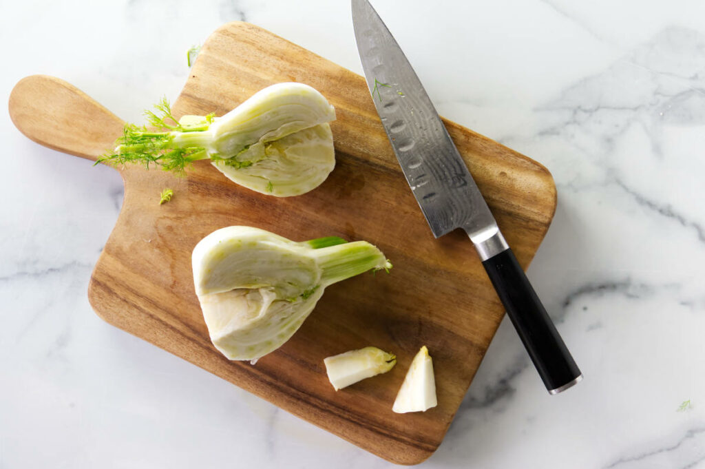 Slicing fresh fennel on a cutting board.