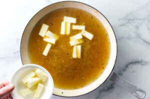 Adding butter to a skillet with chicken broth.