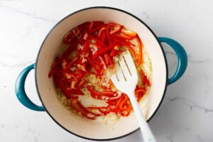 Stirring red bell peppers into a large stock pot.