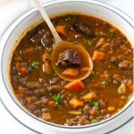 A spoon scooping some lentil beef soup with veggies.