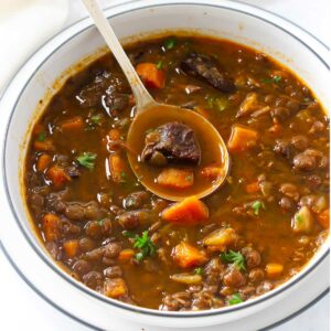 A spoon scooping some lentil beef soup with veggies.