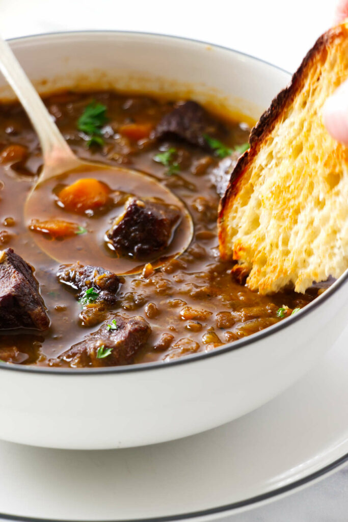 Bread getting dipped into beef lentil soup.