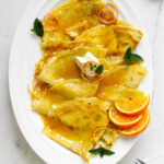Crepes suzette on a platter with orange slices.