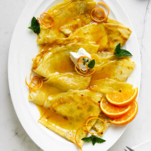 Crepes suzette on a platter with orange slices.