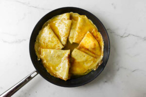 Several crepes in a skillet with orange butter sauce.