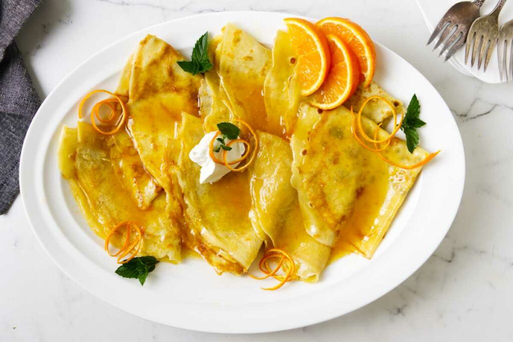 Orange syrup over several crepes on a platter.