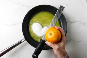 Adding orange zest to a skillet with butter and sugar.