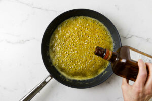 Adding orange liqueur to the orange sauce in the skillet.