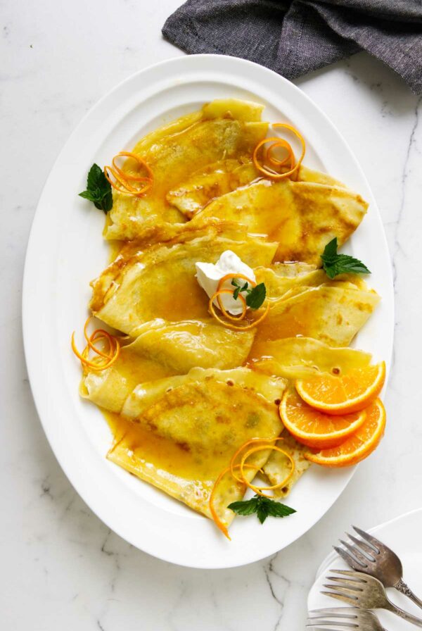 A platter filled with crepes suzette and orange slices.