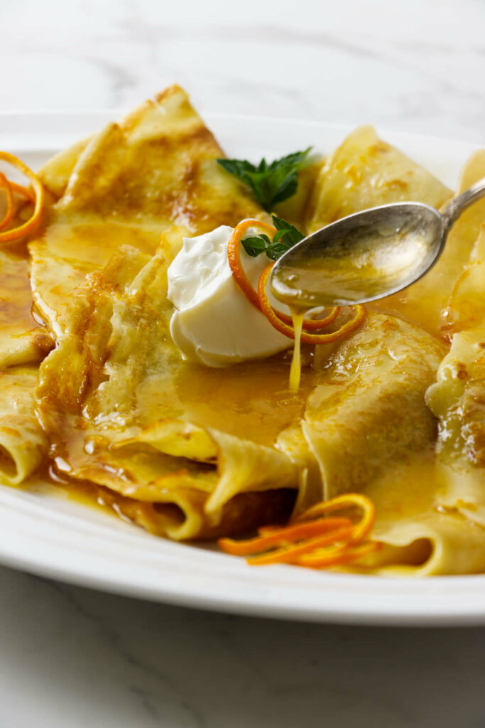 A spoon drizzling orange syrup over crepes.