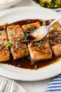 Spooning teriyaki sauce over a platter of salmon.