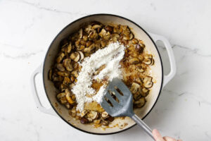 Adding flour to the skillet with mushrooms.