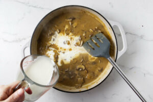 Adding cream to the mushroom sauce.