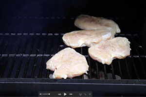 Grilling chicken breasts on a hot grill over coals.