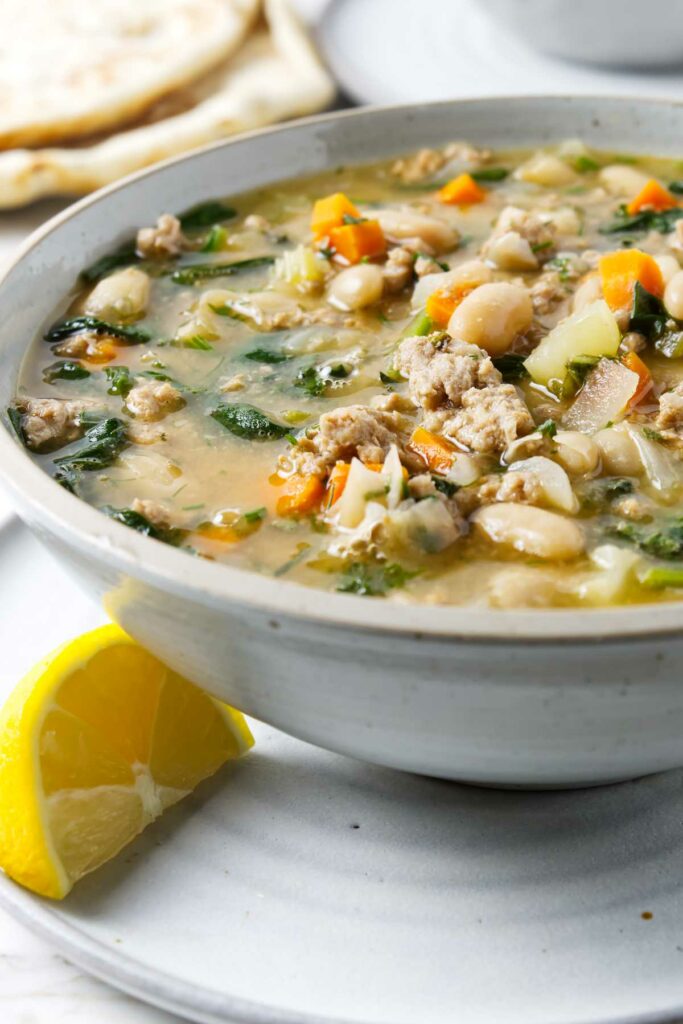A bowl of bean soup next to a wedge of lemon.