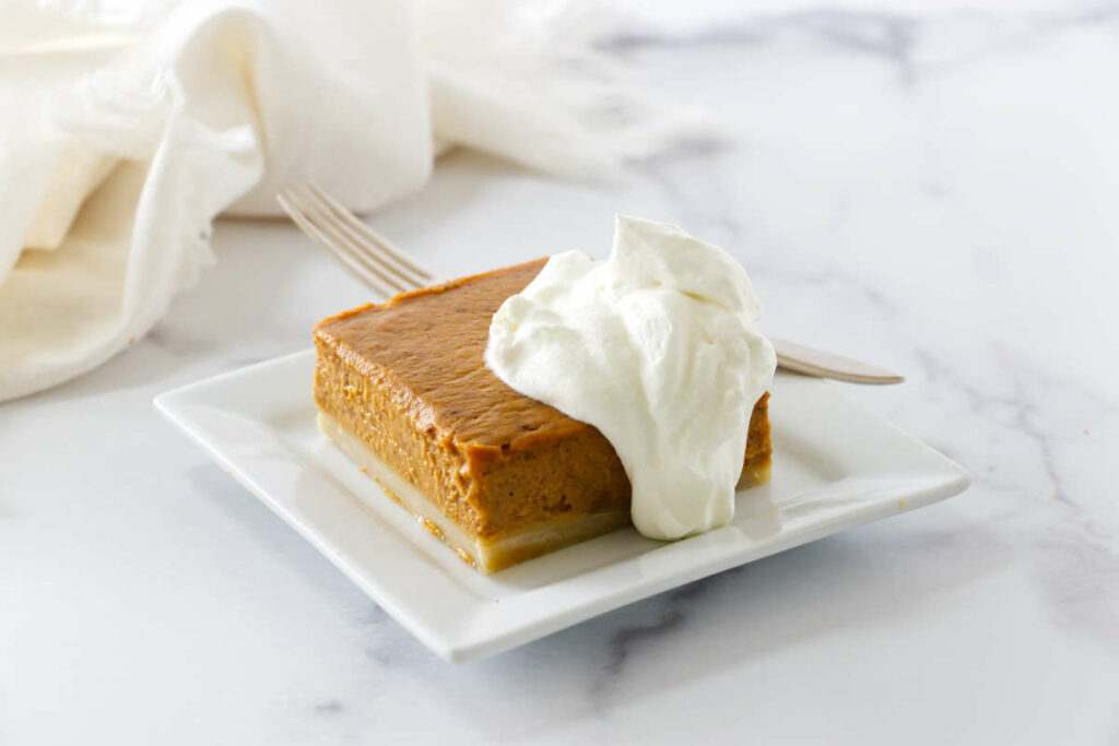 A slice of pumpkin slab pie on a plate with whipped cream.