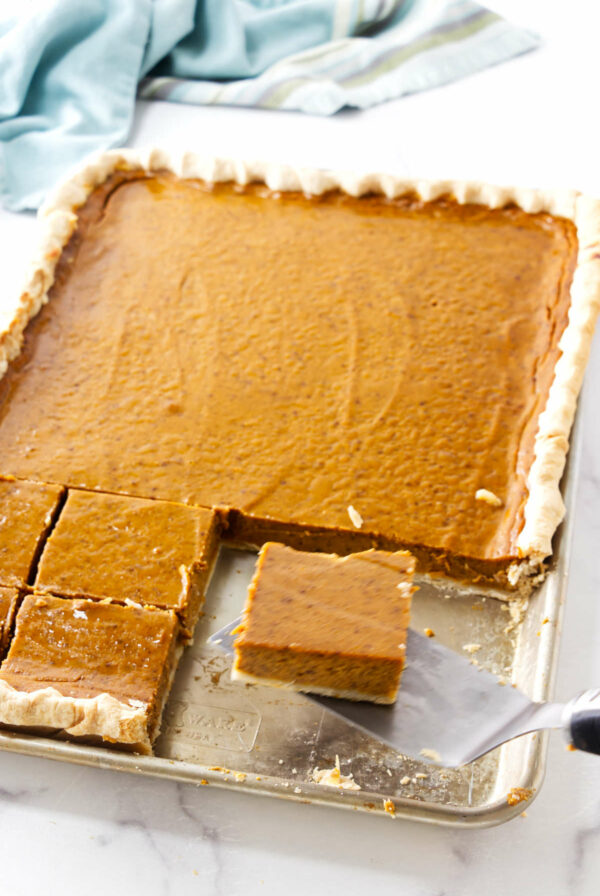 Slices of pumpkin spice pie in a half sheet pan next to a kitchen towel.