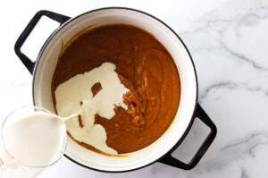 Adding cream to a bowl of pumpkin pie mixture.