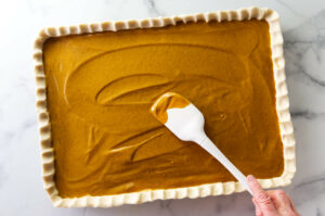 Spreading pumpkin pie custard into a sheet pan lined with pie dough.