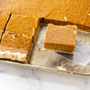 A spatula lifting a slice of pumpkin pie from a sheet pan.