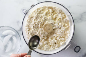 Adding ice water to pie dough in a food processor.