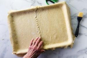 A hand pressing down on the seam in the pie dough.