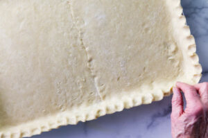 Fingers crimping the edges of the pastry.