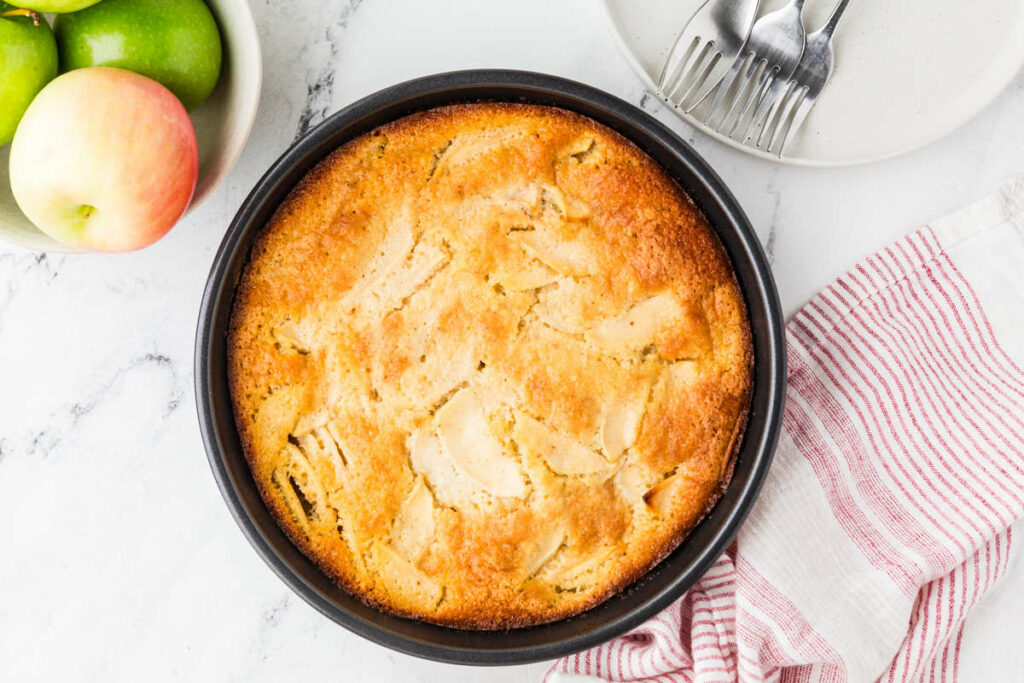 An apple sourdough starter cake in a pan next to apples.