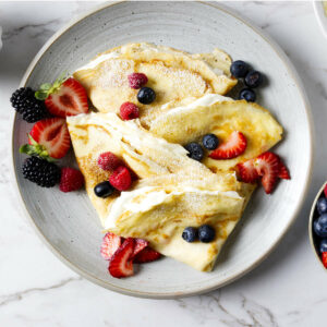 A plate of sourdough crepes with whipped cream and fresh fruit.