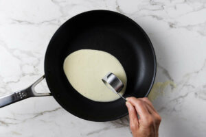 Adding crepe batter to a skillet.