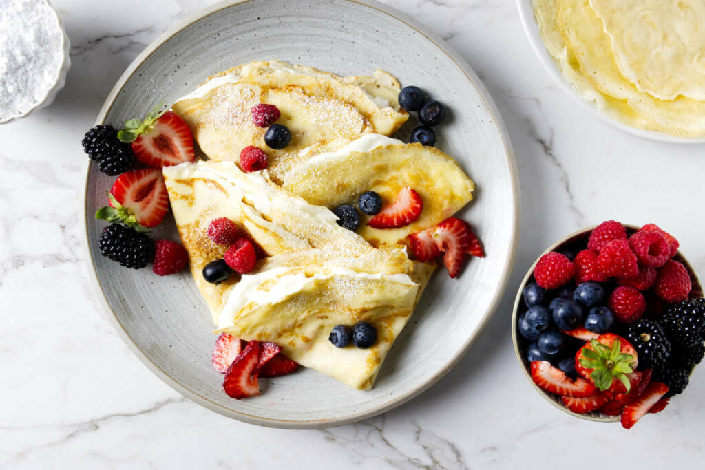 A plate of folded crepes filled with cream and fruit.