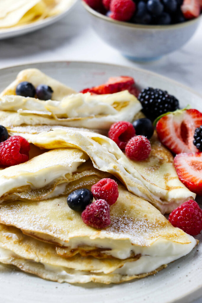 Several sourdough discard crepes filled with whipped cream and fruit.