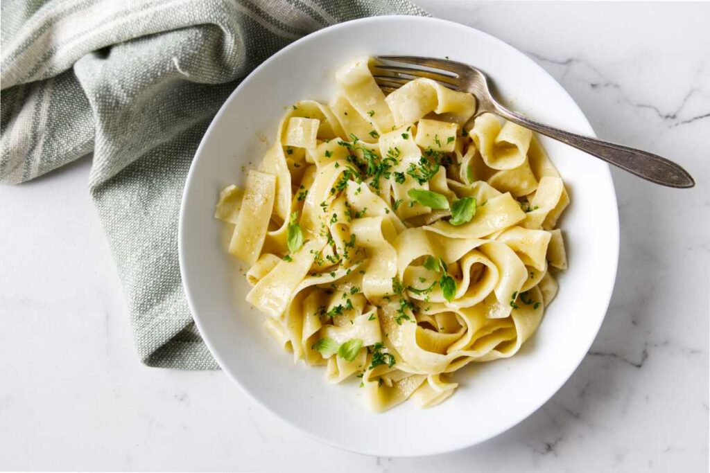 A bowl filled with fresh pasta garnished with chopped herbs.