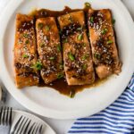 Several fillets of salmon teriyaki on a platter garnished with green onions.