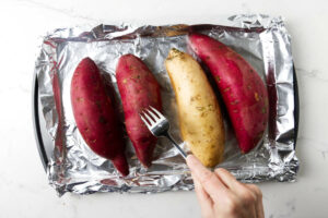 Piercing several sweet potatoes with a fork before baking them.