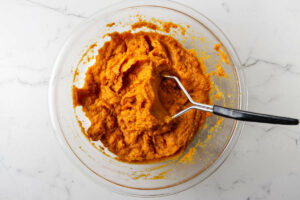 Mashing baked sweet potatoes in a bowl.