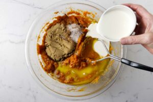 Adding sugar, cream and spices to mashed sweet potatoes in a mixing bowl.