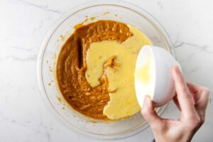 Adding eggs to mashed sweet potato mixture.