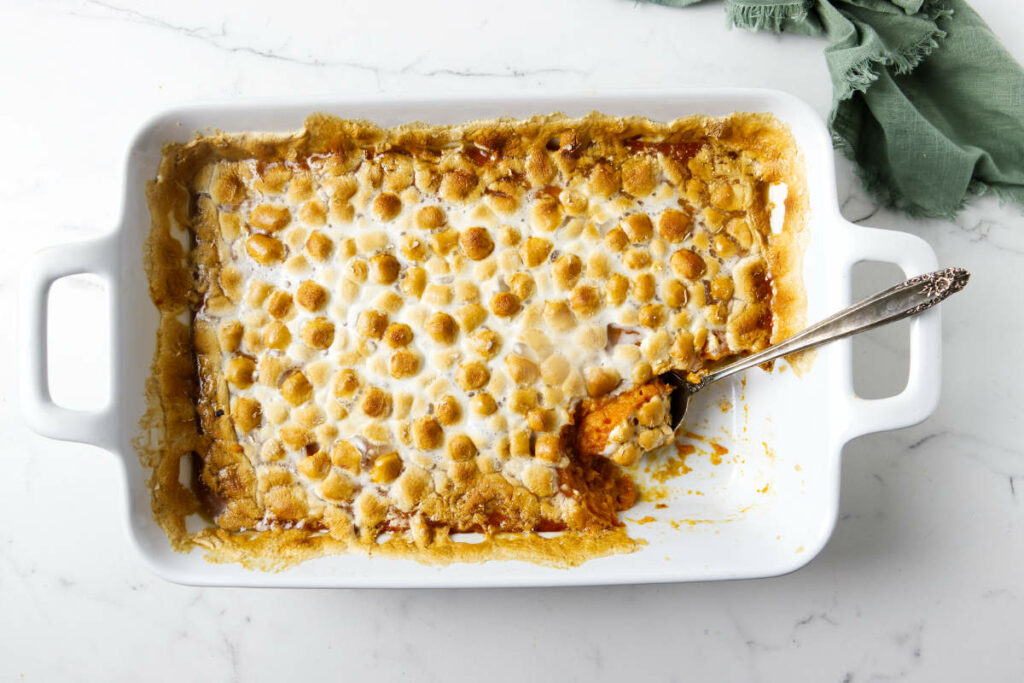 A spoon in a casserole dish with marshmallows and sweet potatoes.