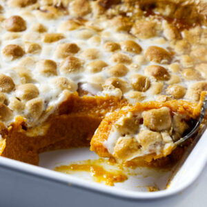 A spoon scooping a serving of sweet potatoes and marshmallows.