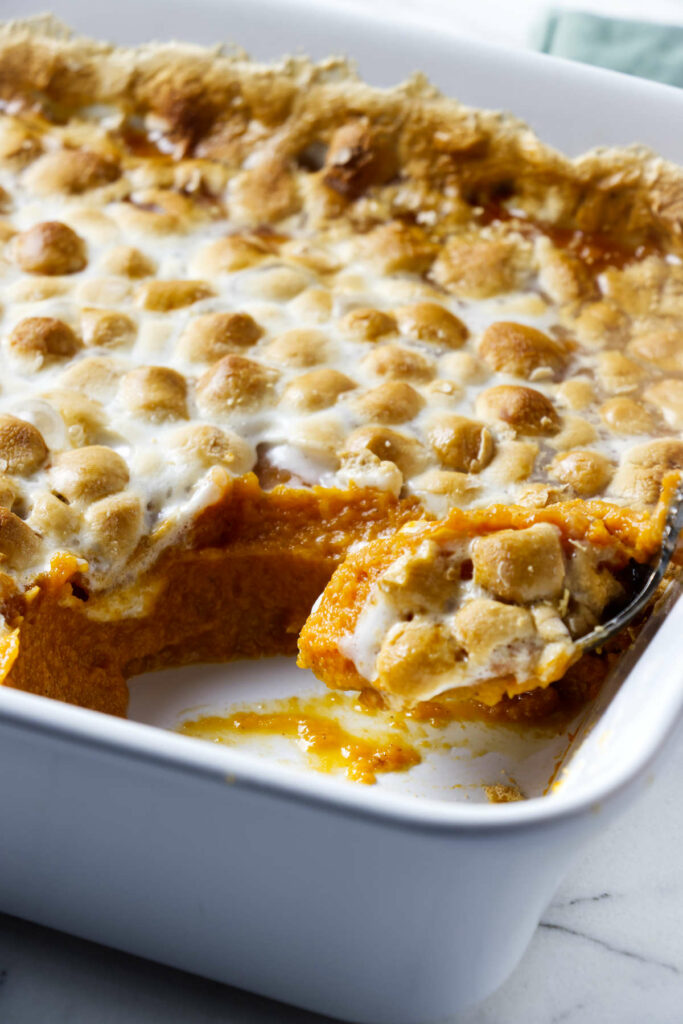 A spoon scooping a serving of sweet potatoes and marshmallows.