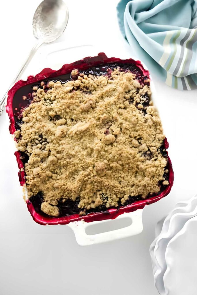 Baked blackberry crumble in white dish with golden topping and bubbling fruit.