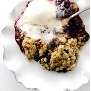 Blackberry crumble with melting vanilla ice cream on a white plate.