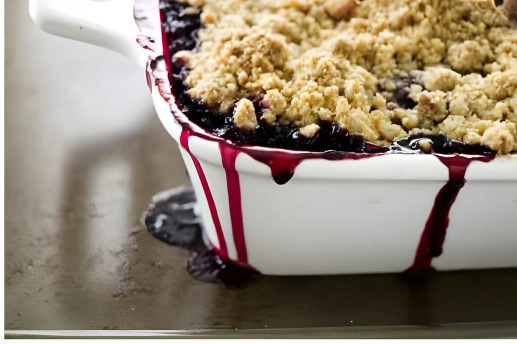 Close-up of blackberry crumble in white dish, juice bubbling over edge.